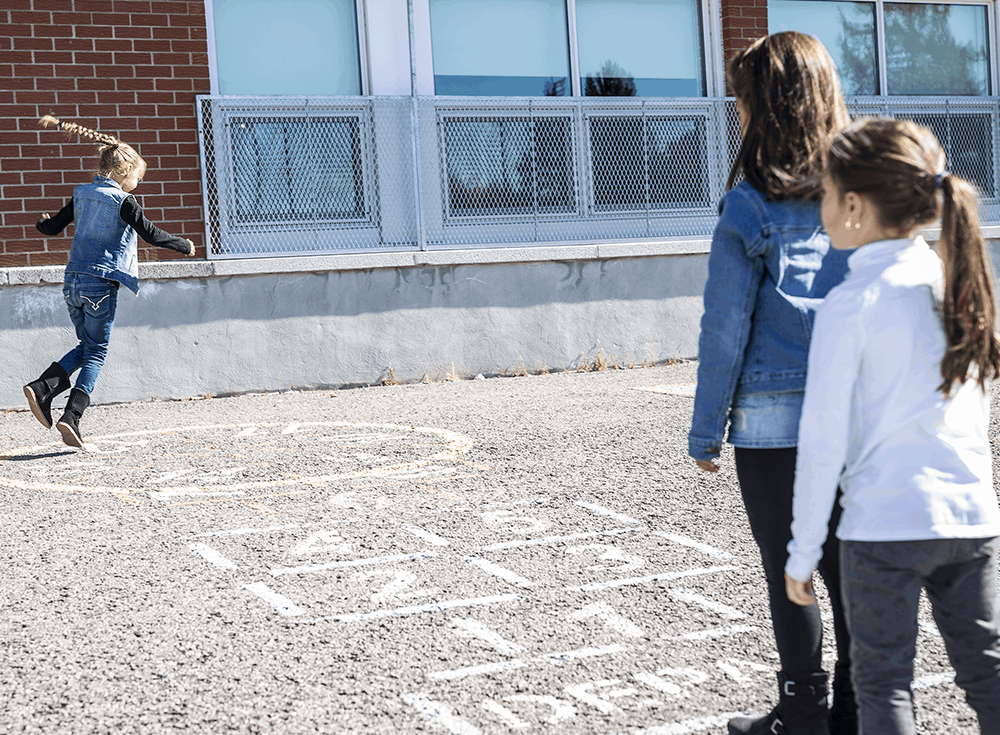 3 children playing hopscotch on a school playground
